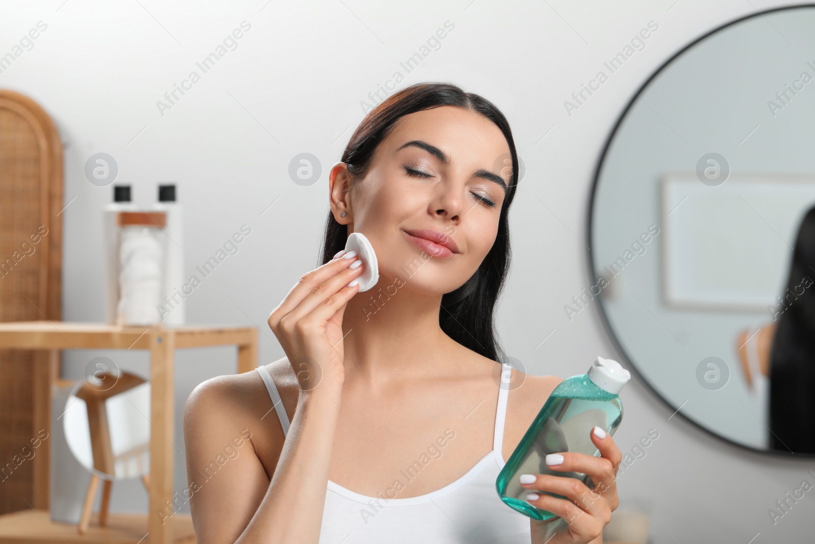 Photo of Young woman using cotton pad with micellar water indoors