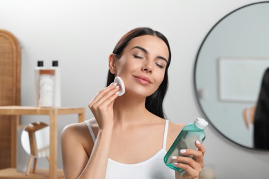 Young woman using cotton pad with micellar water indoors