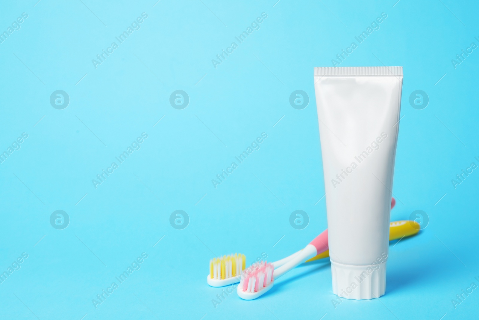 Photo of Blank tube of toothpaste and brushes on color background. Space for text