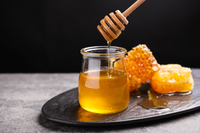 Honey dripping from dipper into jar on grey table