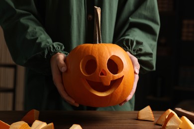 Woman holding carved pumpkin for Halloween at wooden table, closeup