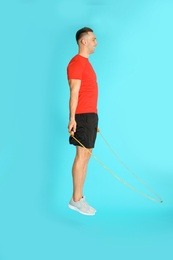 Photo of Young sportive man training with jump rope on color background