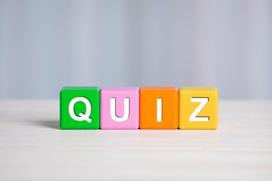 Photo of Colorful cubes with word Quiz on white wooden table. Space for text