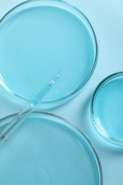 Measuring pipette and petri dishes on light blue table, flat lay