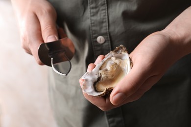 Photo of Man holding fresh oyster and knife on beige background, closeup
