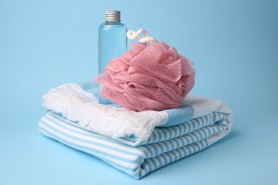 Photo of Pink shower puff, bottle of cosmetic product and towel on light blue background