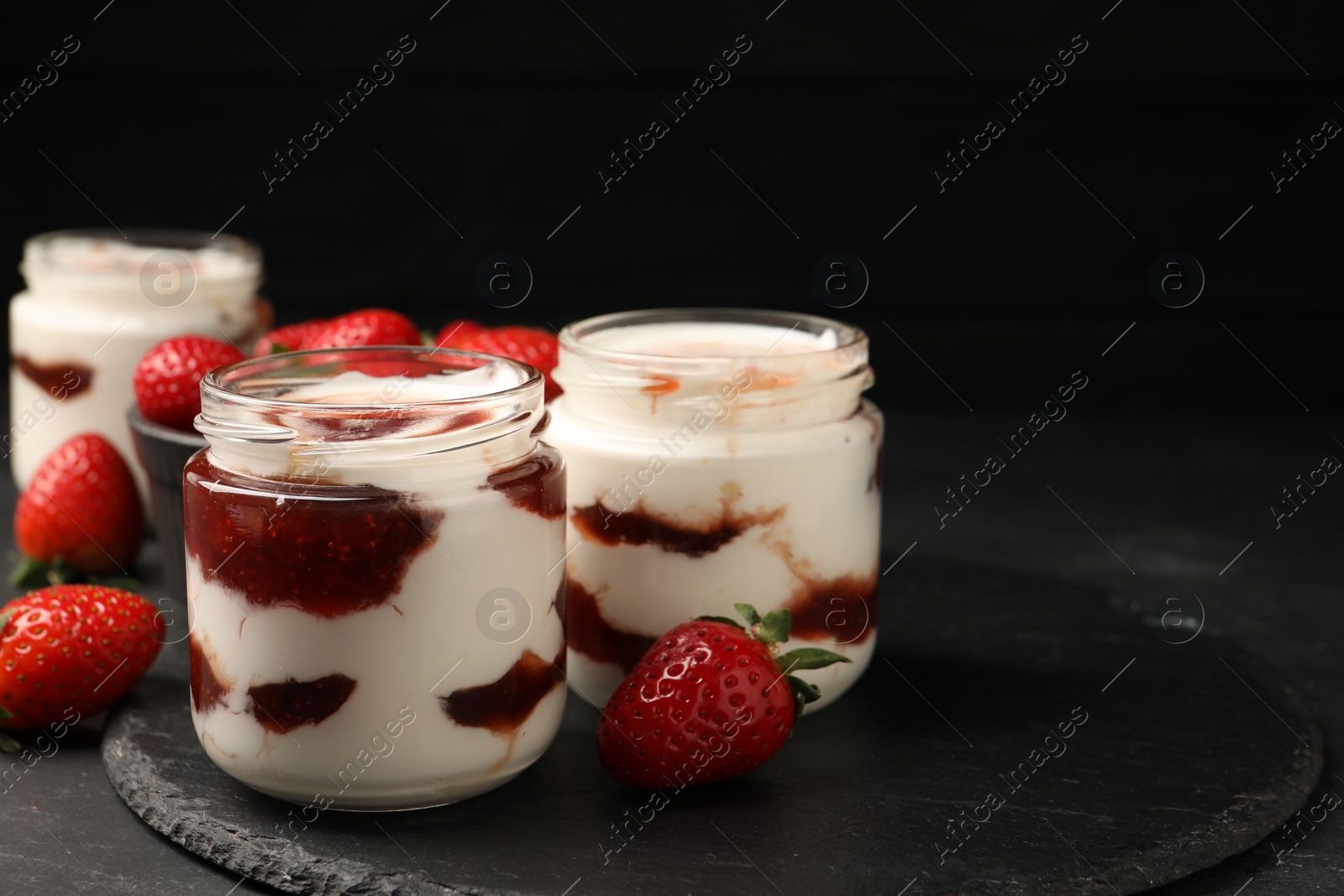 Photo of Tasty yoghurt with jam and strawberries on black table, closeup. Space for text