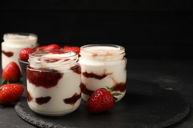 Photo of Tasty yoghurt with jam and strawberries on black table, closeup. Space for text