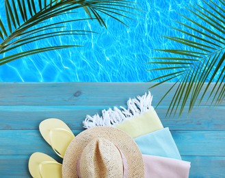 Beach accessories on light blue wooden surface near swimming pool, above view