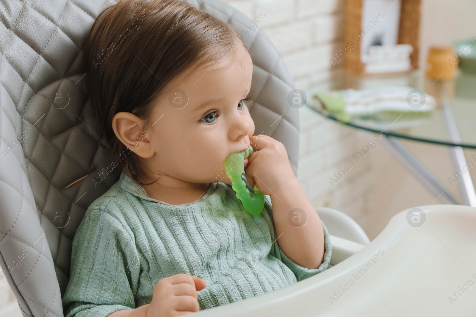 Photo of Cute little baby nibbling teether in high chair indoors. Space for text