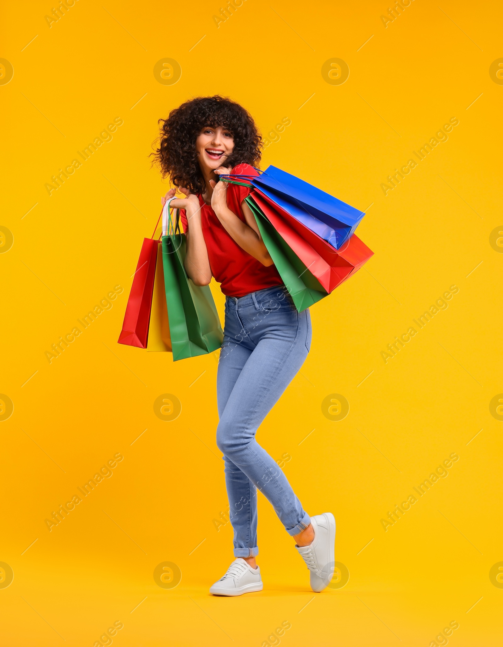 Photo of Happy young woman with shopping bags on yellow background