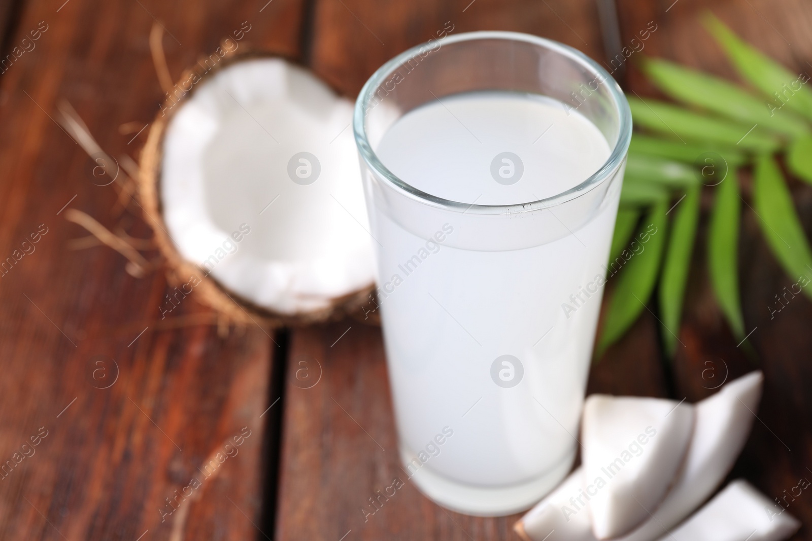 Photo of Glass of coconut water, leaf and nuts on wooden table, space for text