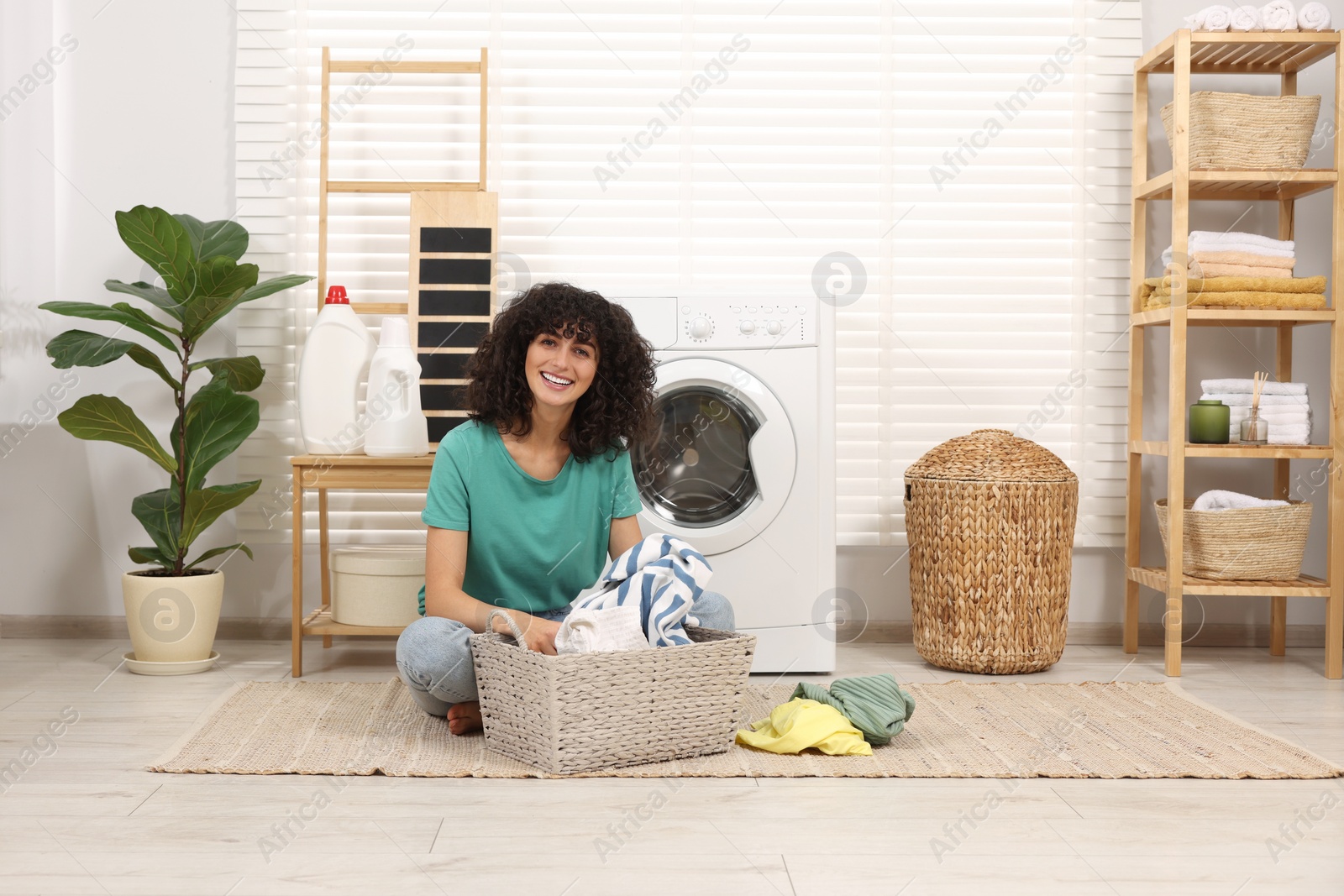 Photo of Happy woman with laundry near washing machine indoors