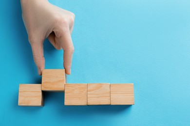 Photo of Woman arranging blank wooden cubes on light blue background, top view. Space for text