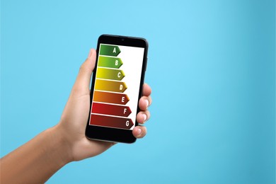 Image of Energy efficiency rating on smartphone display. Man holding device on light blue background, closeup