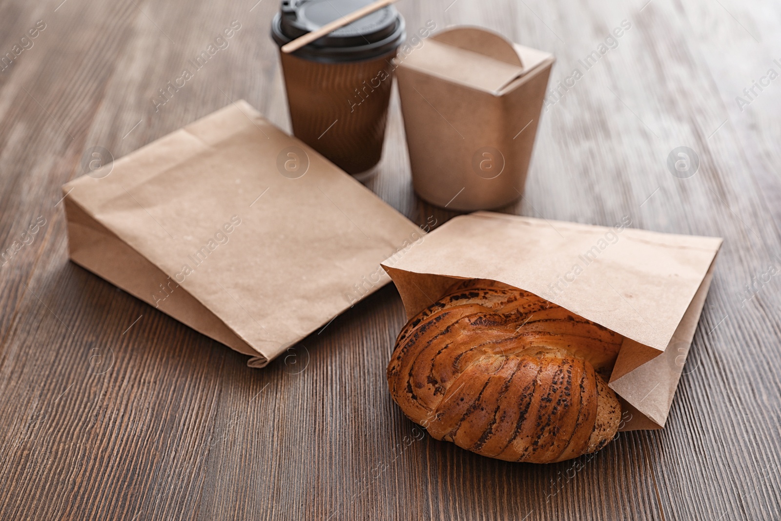 Photo of Takeaway food in paper bags and coffee on wooden table