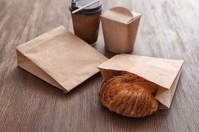 Takeaway food in paper bags and coffee on wooden table
