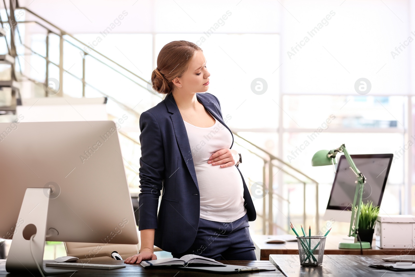 Photo of Young pregnant woman suffering from pain while working in office