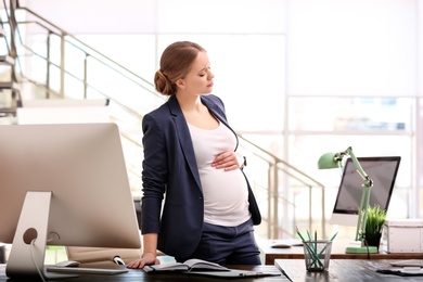 Photo of Young pregnant woman suffering from pain while working in office