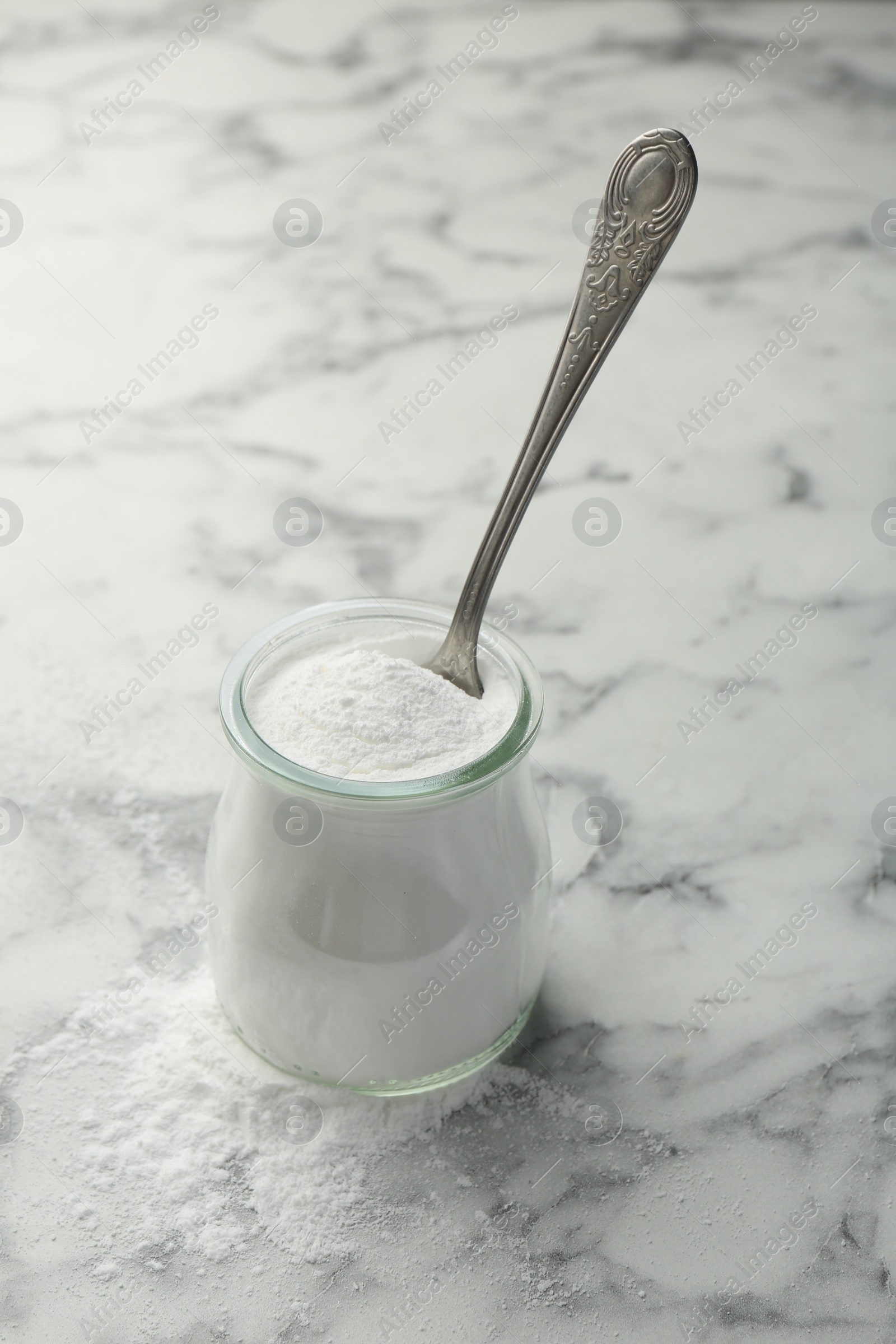 Photo of Baking powder in jar and spoon on white marble table