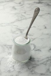 Baking powder in jar and spoon on white marble table