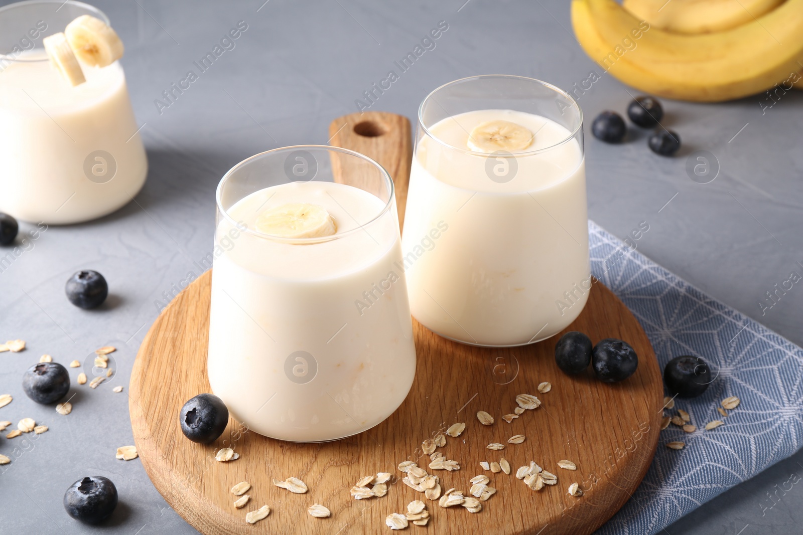 Photo of Tasty yogurt in glasses, oats and blueberries on grey table