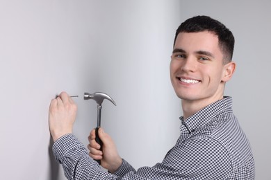 Photo of Young man hammering nail into white wall indoors