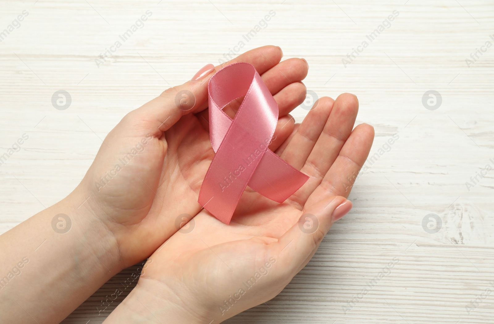 Photo of Woman with pink ribbon at white wooden table, closeup. Breast cancer awareness