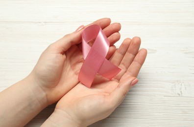 Woman with pink ribbon at white wooden table, closeup. Breast cancer awareness