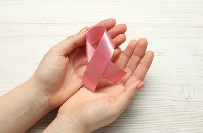 Photo of Woman with pink ribbon at white wooden table, closeup. Breast cancer awareness