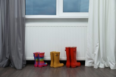 Photo of Rubber boots near heating radiator in room