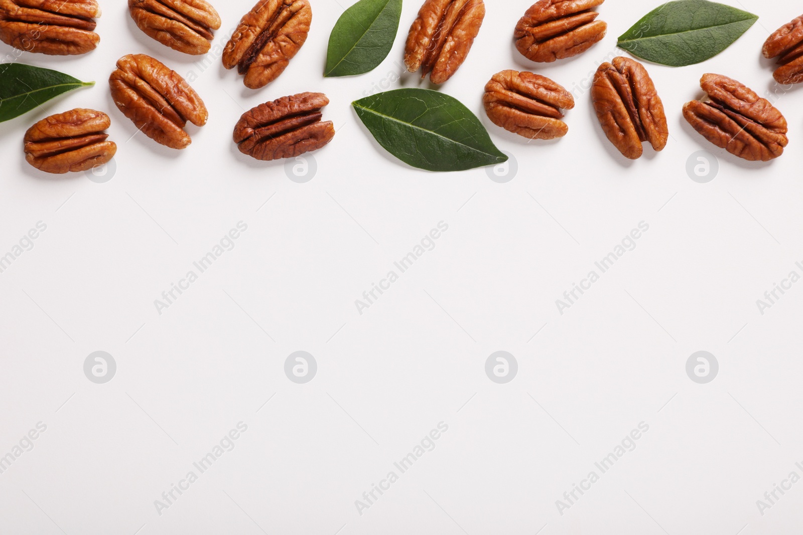 Photo of Delicious pecan nuts and green leaves on white background, flat lay. Space for text