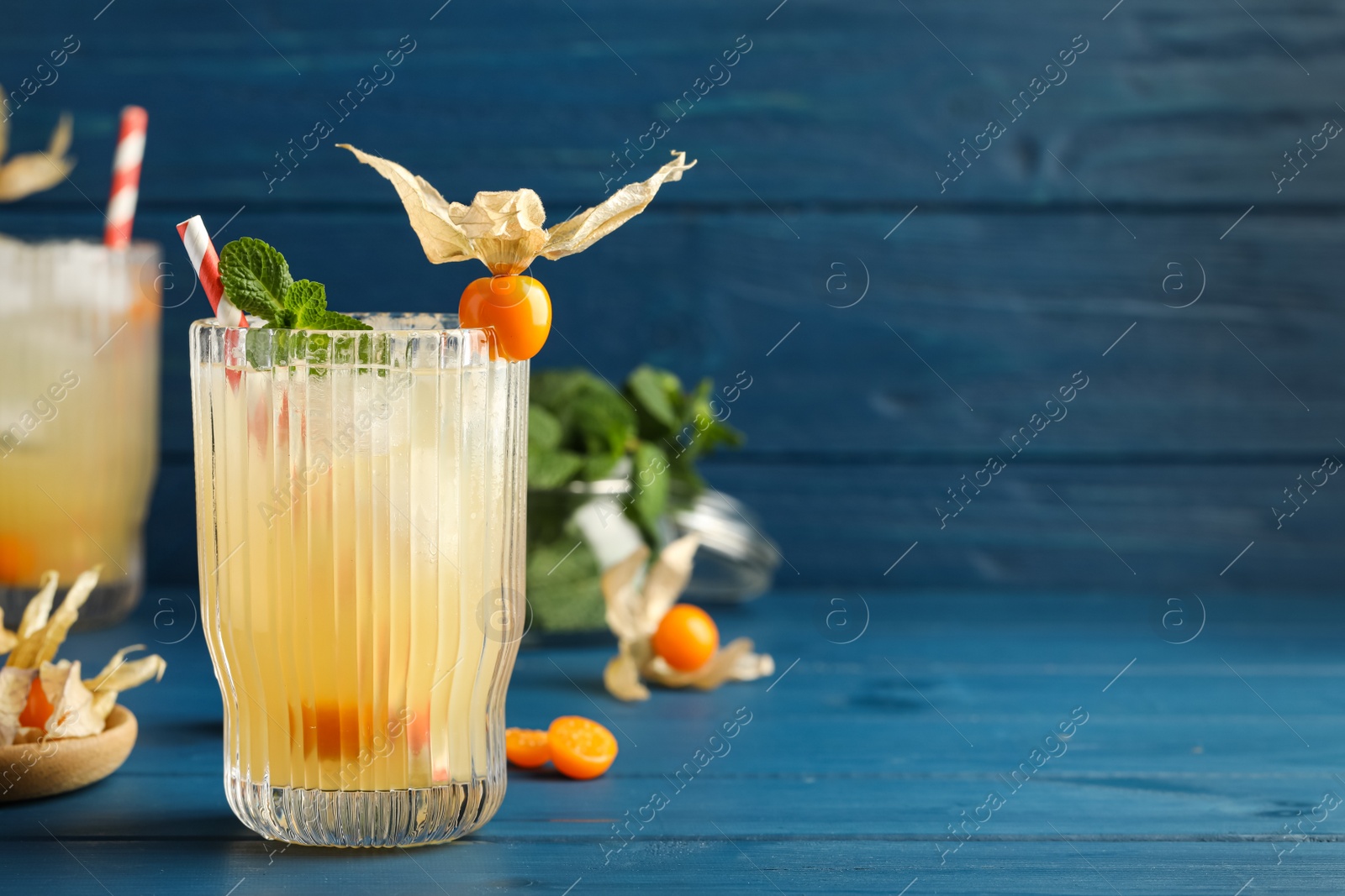 Photo of Refreshing cocktail decorated with physalis fruit on blue wooden table. Space for text