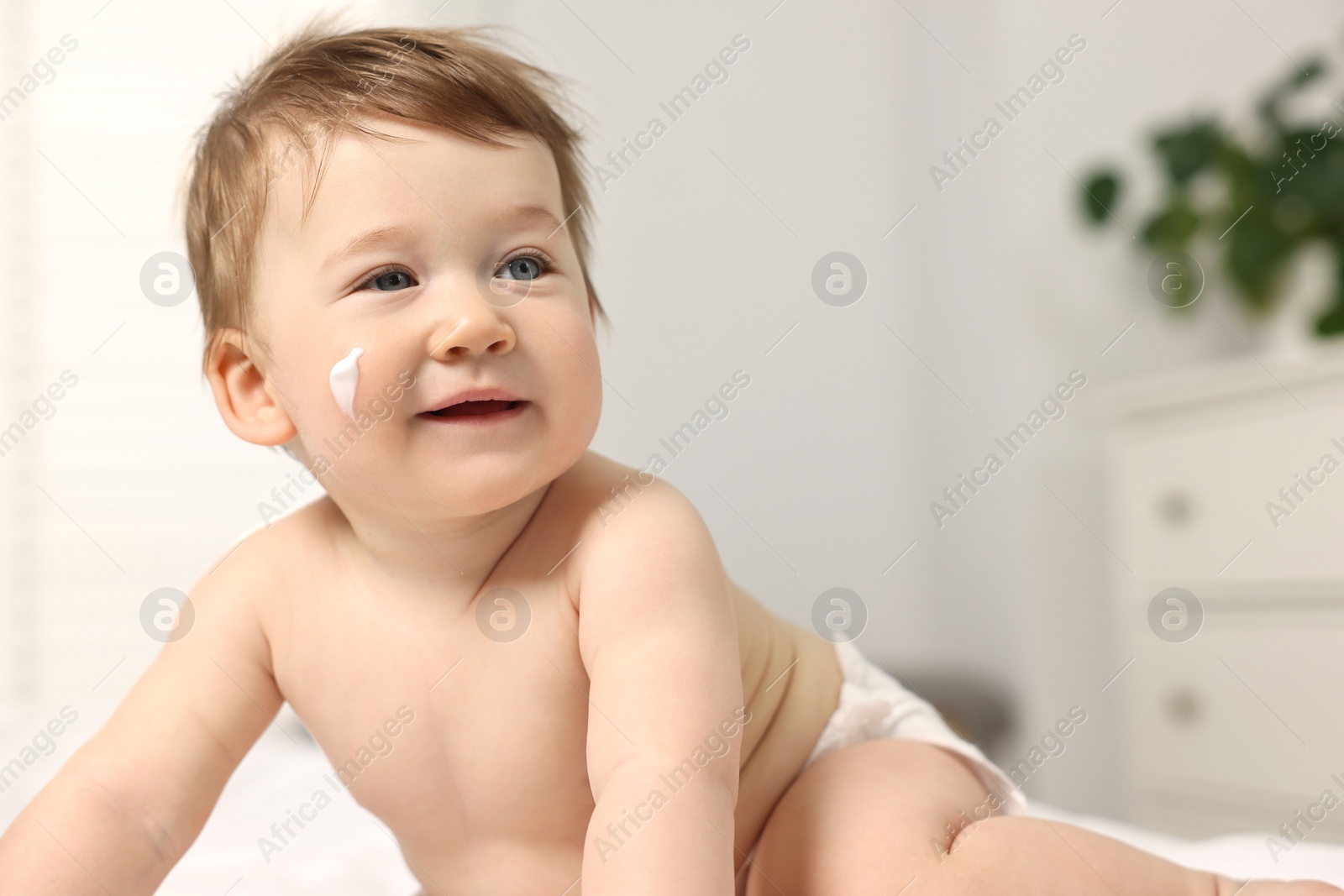 Photo of Cute little baby with moisturizing cream on face indoors