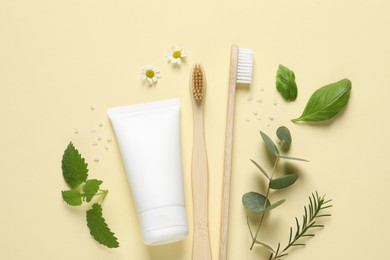 Photo of Flat lay composition with bamboo toothbrushes, tube of cream and herbs on beige background