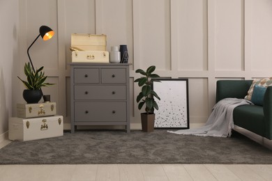 Photo of Stylish room interior with storage trunks, grey chest of drawers and comfortable sofa