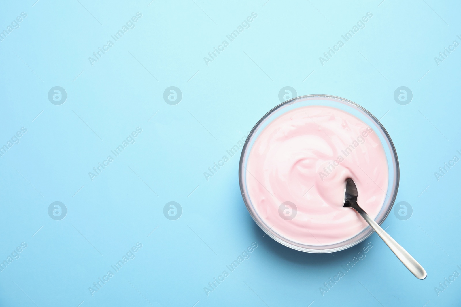 Photo of Glass bowl with creamy yogurt and spoon on color background, top view. Space for text