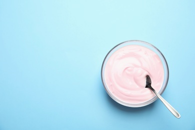 Photo of Glass bowl with creamy yogurt and spoon on color background, top view. Space for text