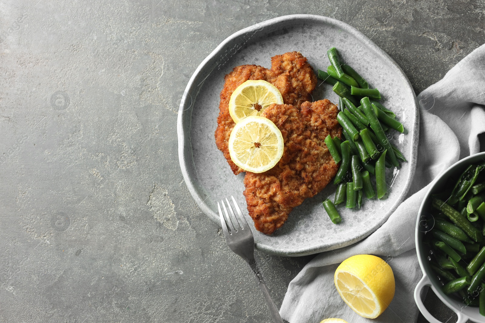 Photo of Tasty schnitzels served with lemon and green beans on grey table, flat lay. Space for text