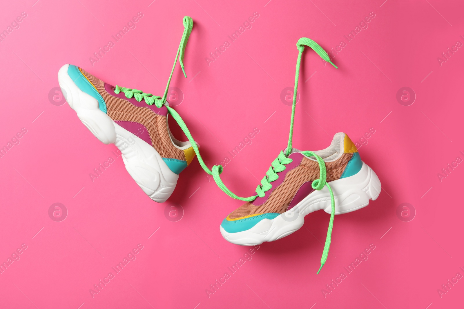 Photo of Stylish sneakers with green shoe laces hanging on pink wall