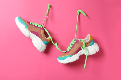 Photo of Stylish sneakers with green shoe laces hanging on pink wall