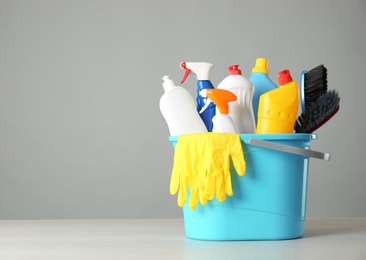 Photo of Bucket with cleaning products and tools on grey table. Space for text