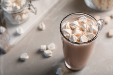 Tasty hot chocolate with milk and marshmallows in glass cup on table. Space for text