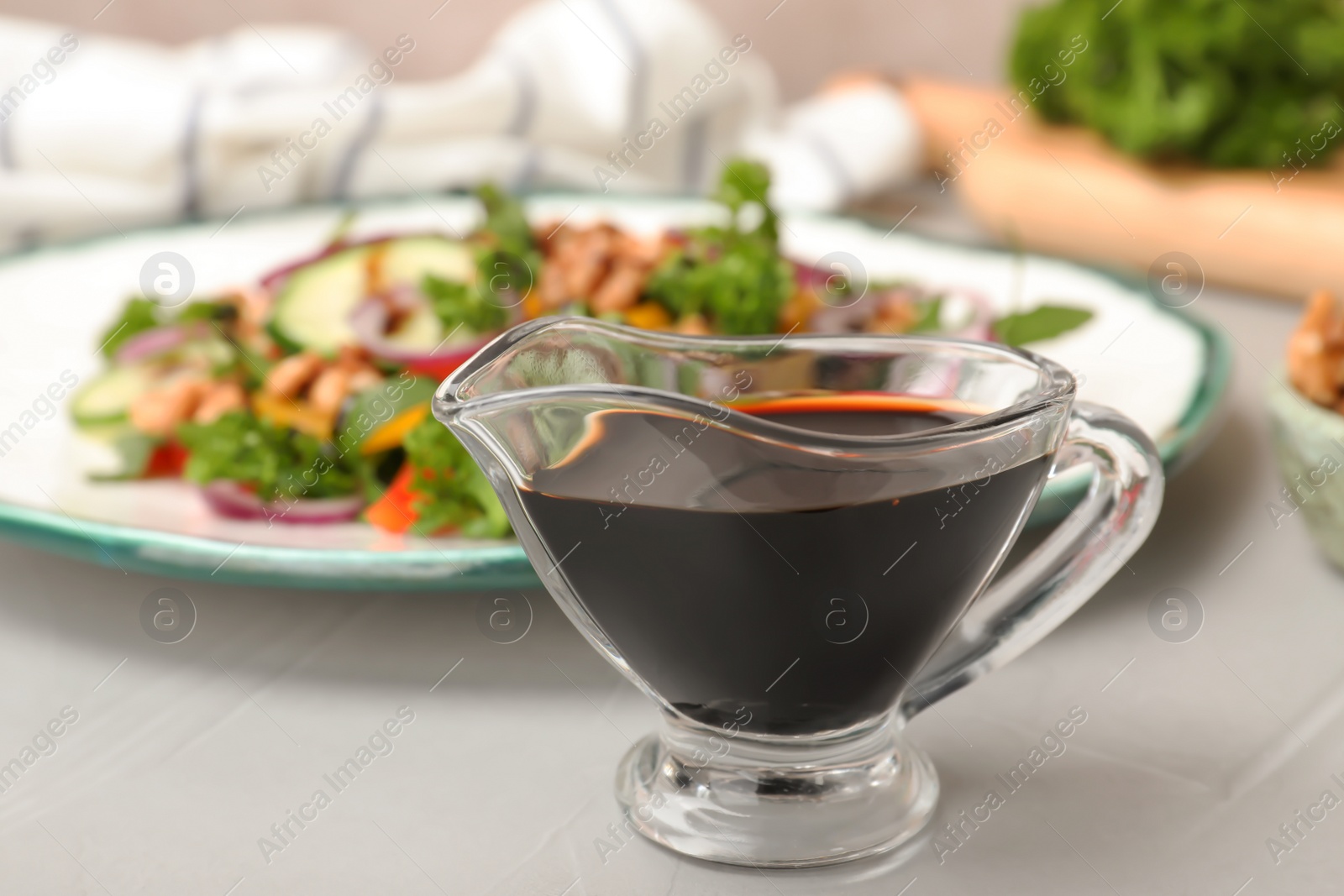 Photo of Balsamic vinegar in gravy boat near plate with salad on table