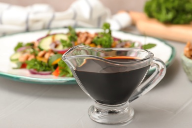 Photo of Balsamic vinegar in gravy boat near plate with salad on table