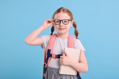 Cute girl with book and backpack on light blue background