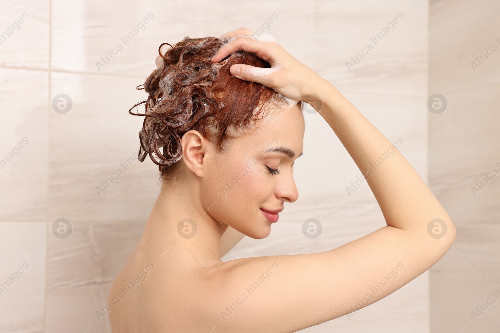 Photo of Happy young woman washing her hair with shampoo in shower