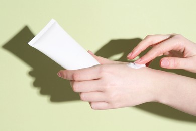 Woman with tube applying cream on her hand against green background, closeup