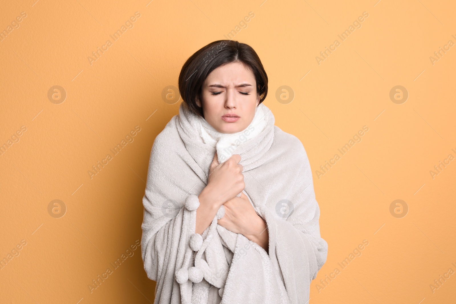 Photo of Young woman wrapped in blanket suffering from cold on color background