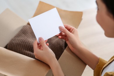 Photo of Woman holding greeting card near parcel with Christmas gift indoors, closeup